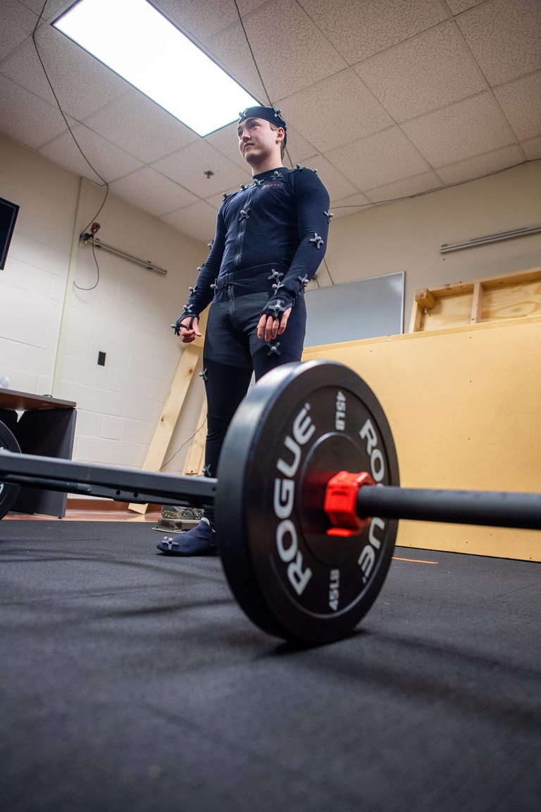 Person in a motion suit preparing to lift a barbell