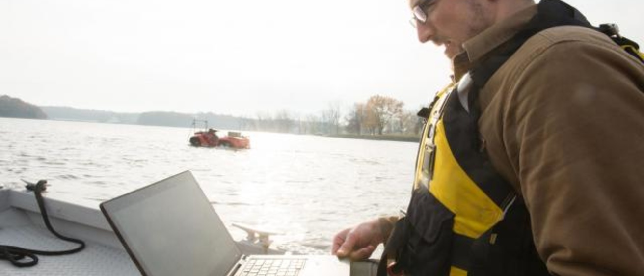 IIHR—Hydroscience and Engineering researcher Casey Harwood peruses data from an amphibious Gibbs Quadski (seen in the distance) at the Coralville Reservoir