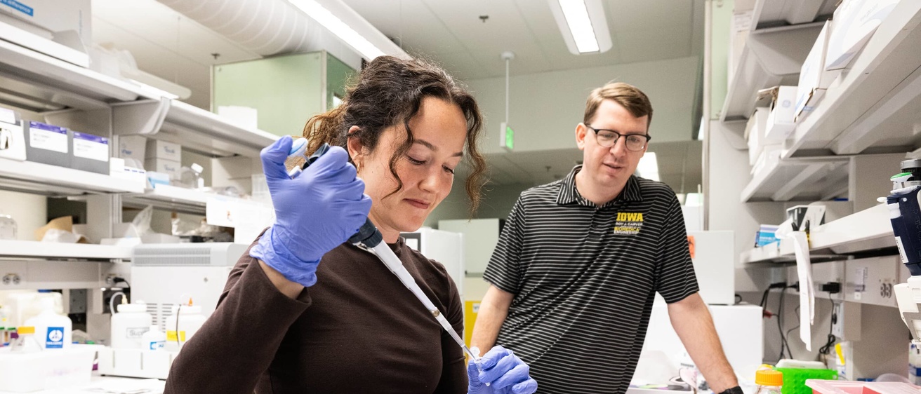A professor watches a student work in the lab