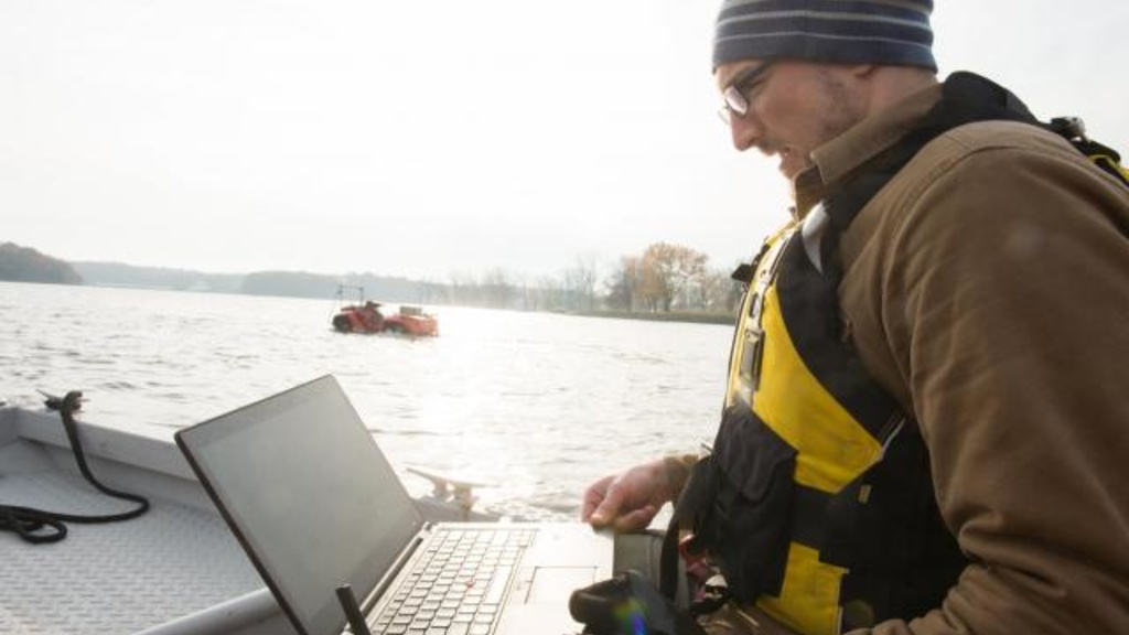 IIHR—Hydroscience and Engineering researcher Casey Harwood peruses data from an amphibious Gibbs Quadski (seen in the distance) at the Coralville Reservoir