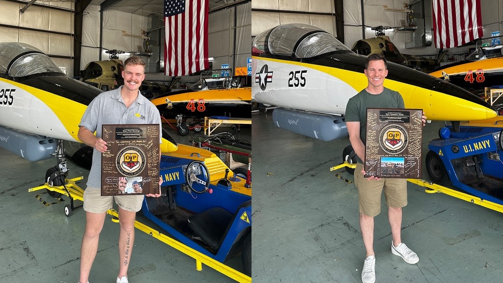 Two students pose for photos in an airplane hangar